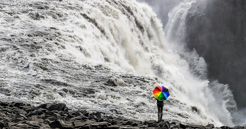Uomo con un ombrello colorato e una cascata
